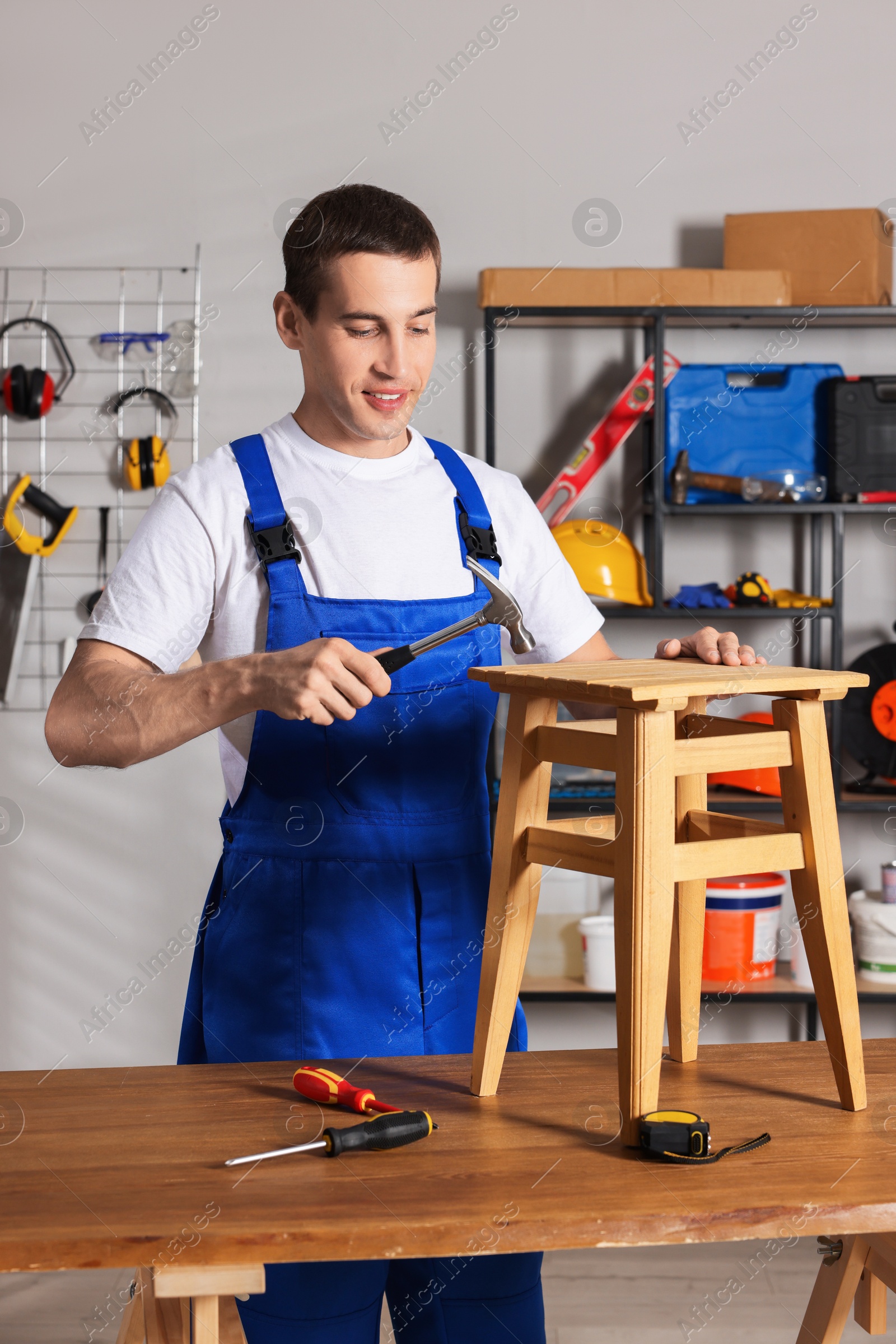 Photo of Man repairing wooden stool with hammer indoors