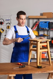 Man repairing wooden stool with hammer indoors