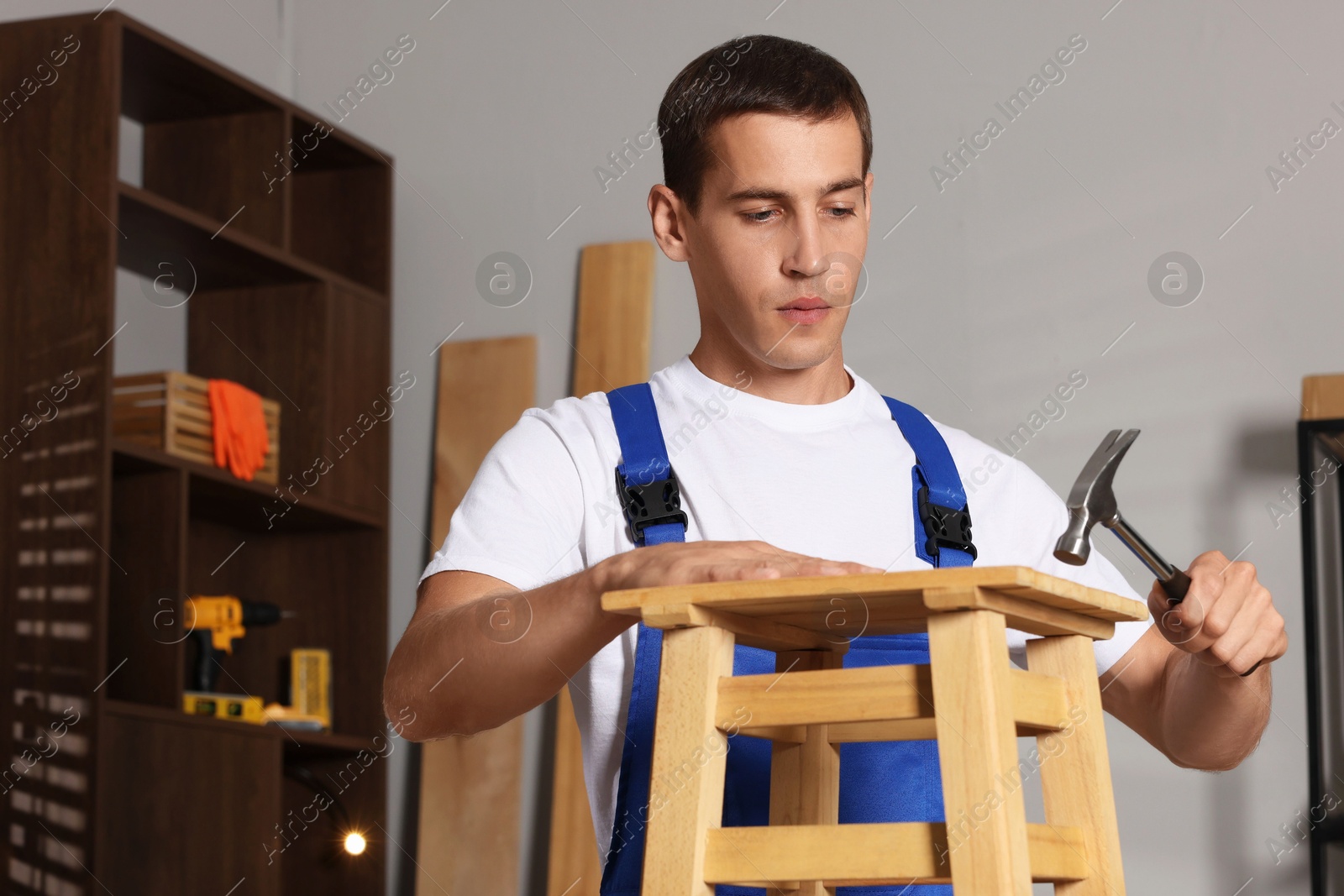 Photo of Man repairing wooden stool with hammer indoors