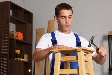 Photo of Man repairing wooden stool with hammer indoors