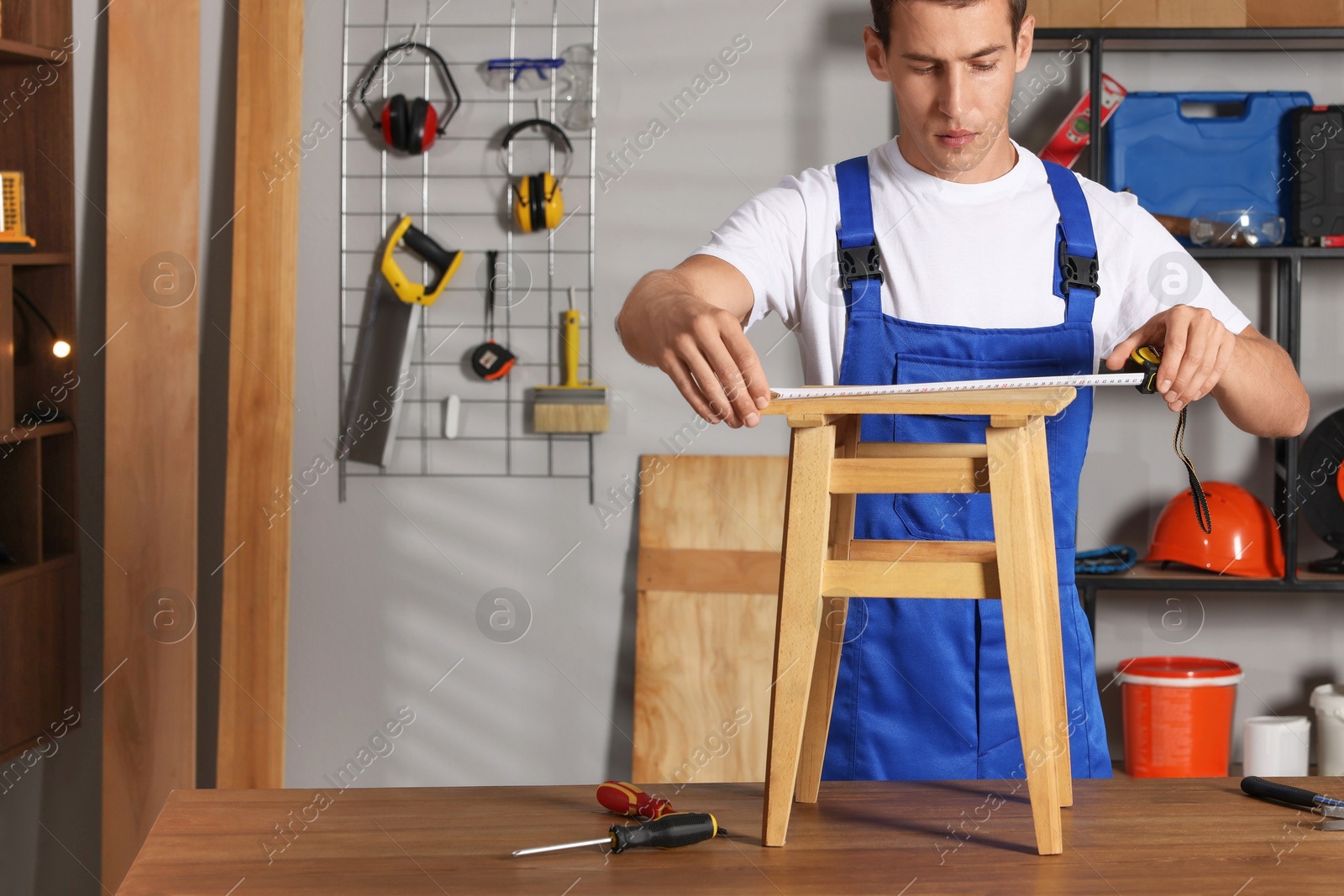 Photo of Man using tape measure while repairing wooden stool indoors