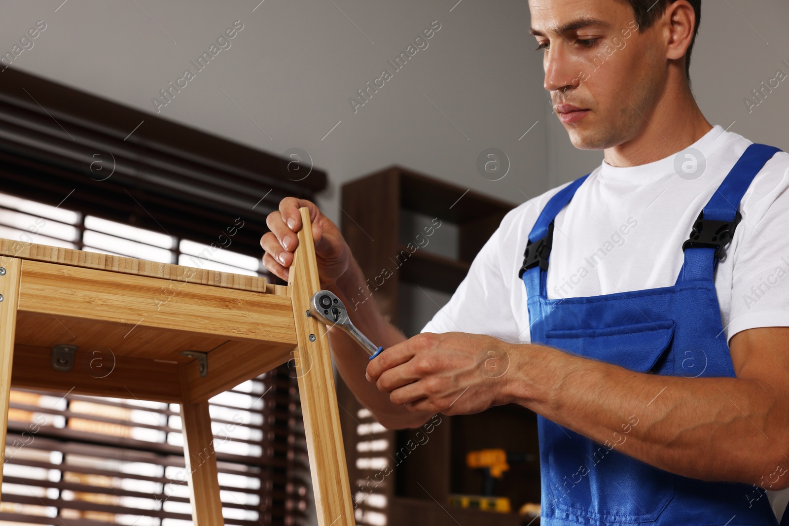 Photo of Man repairing wooden stool with torque wrench indoors