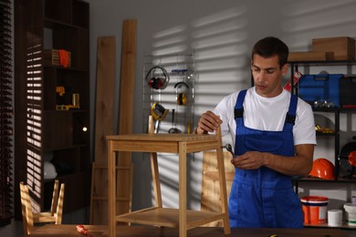 Man repairing wooden stool with torque wrench indoors