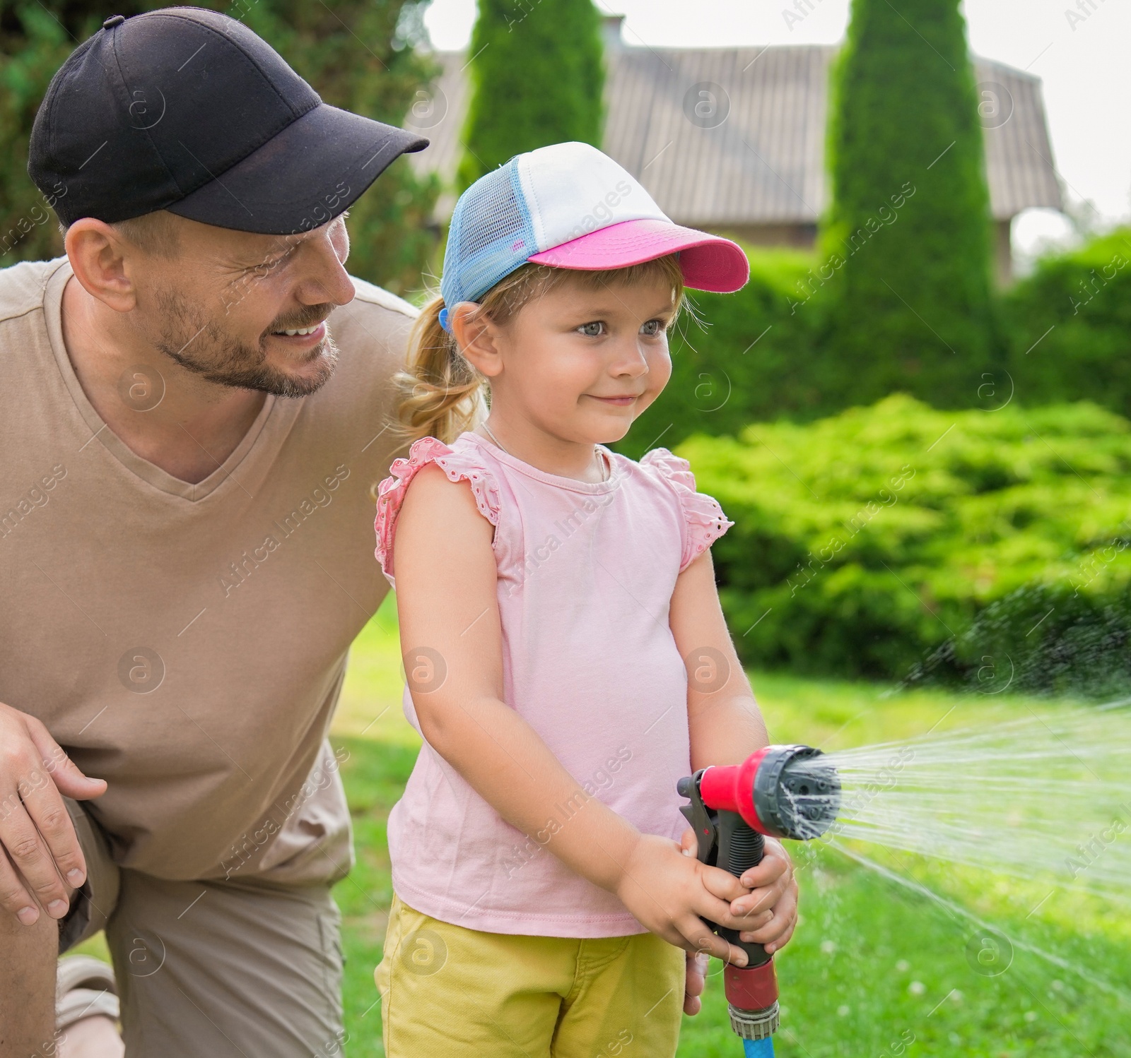 Photo of Father and his daughter watering lawn with hose in backyard