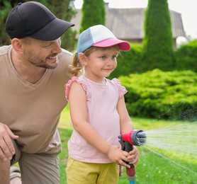 Father and his daughter watering lawn with hose in backyard