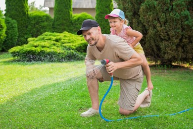 Photo of Father and his daughter watering lawn with hose in backyard