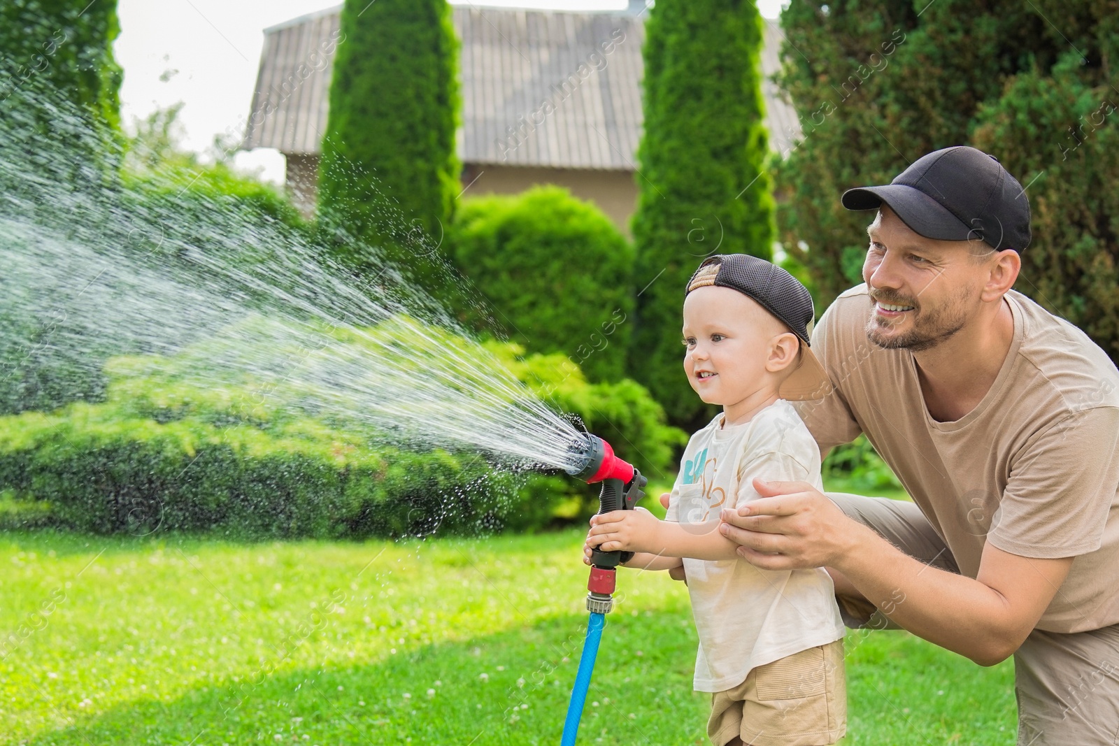 Photo of Father and his son watering lawn with hose in backyard