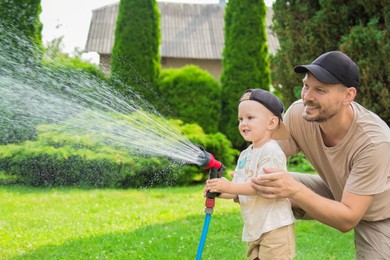 Father and his son watering lawn with hose in backyard