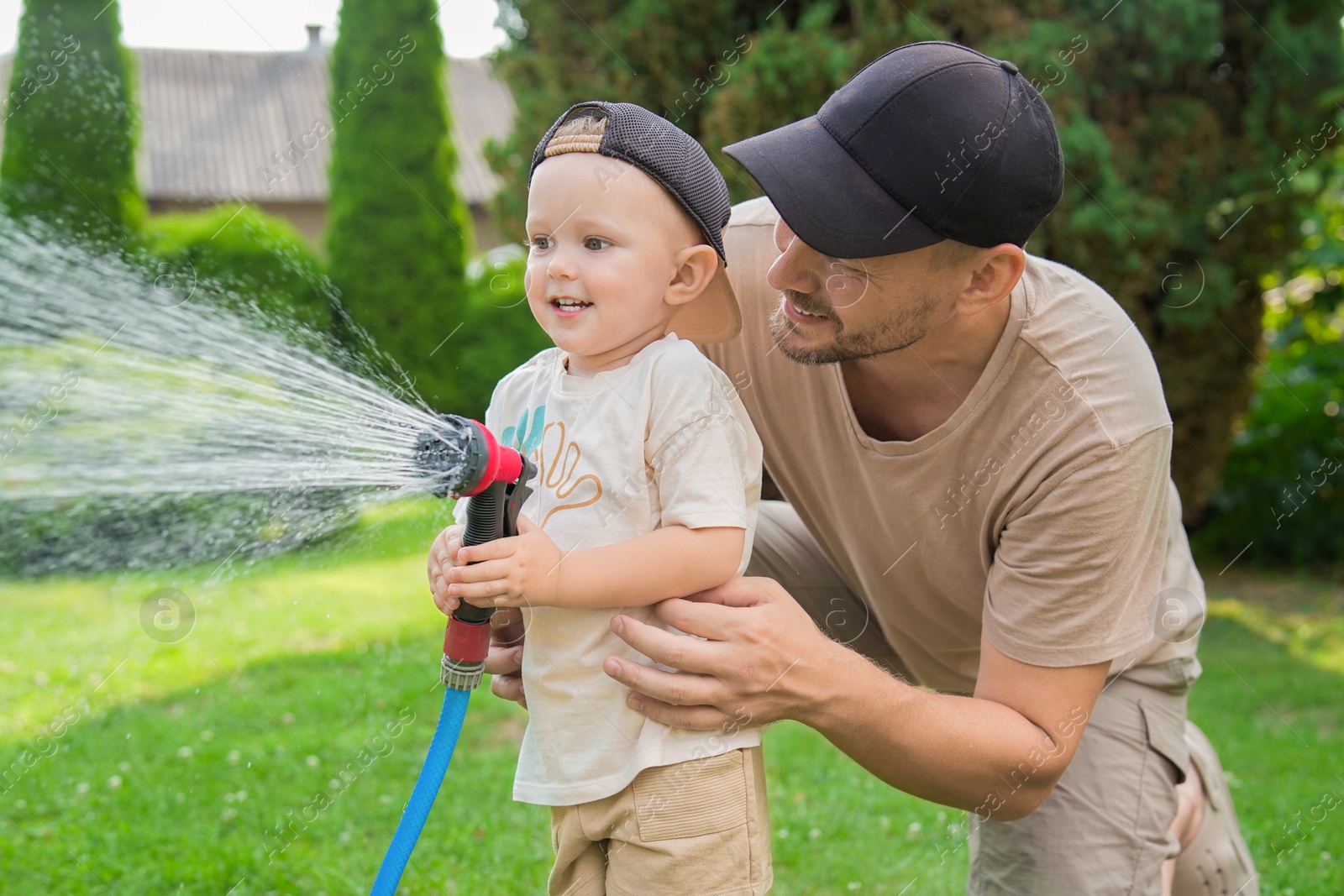 Photo of Father and his son watering lawn with hose in backyard