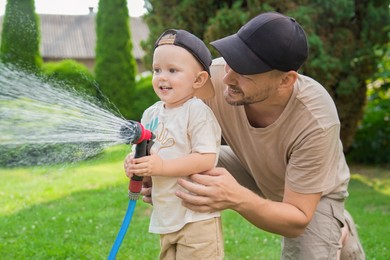 Father and his son watering lawn with hose in backyard