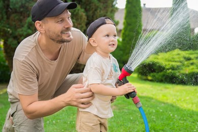 Father and his son watering lawn with hose in backyard