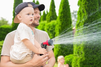 Photo of Father and his son watering lawn with hose in backyard