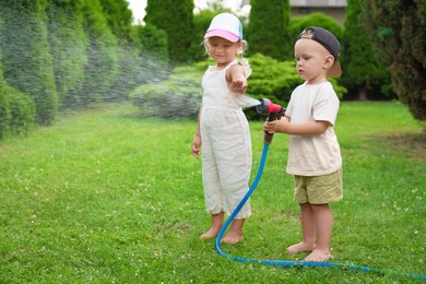 Little boy and his sister watering lawn with hose in backyard