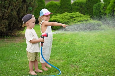 Little boy and his sister watering lawn with hose in backyard