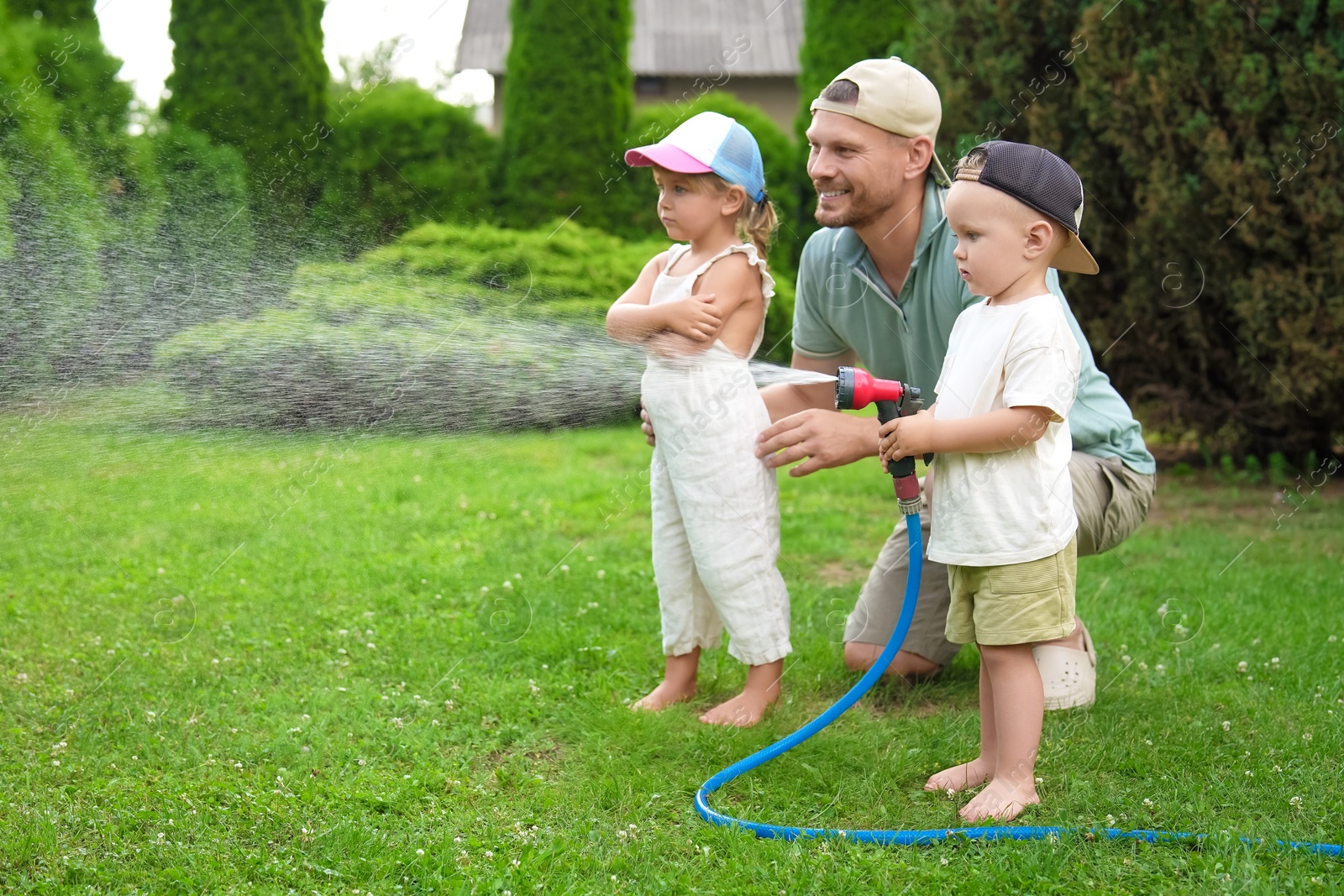 Photo of Father and his kids watering lawn with hose in backyard