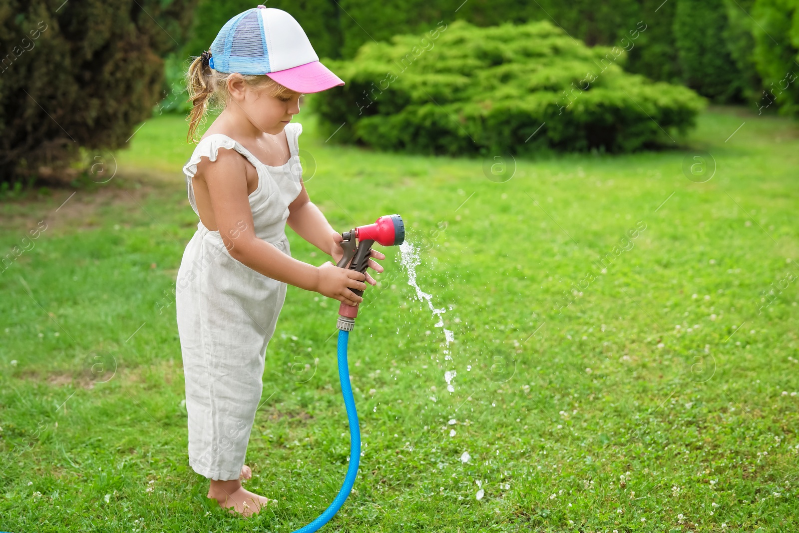 Photo of Little girl watering lawn with hose in backyard, space for text