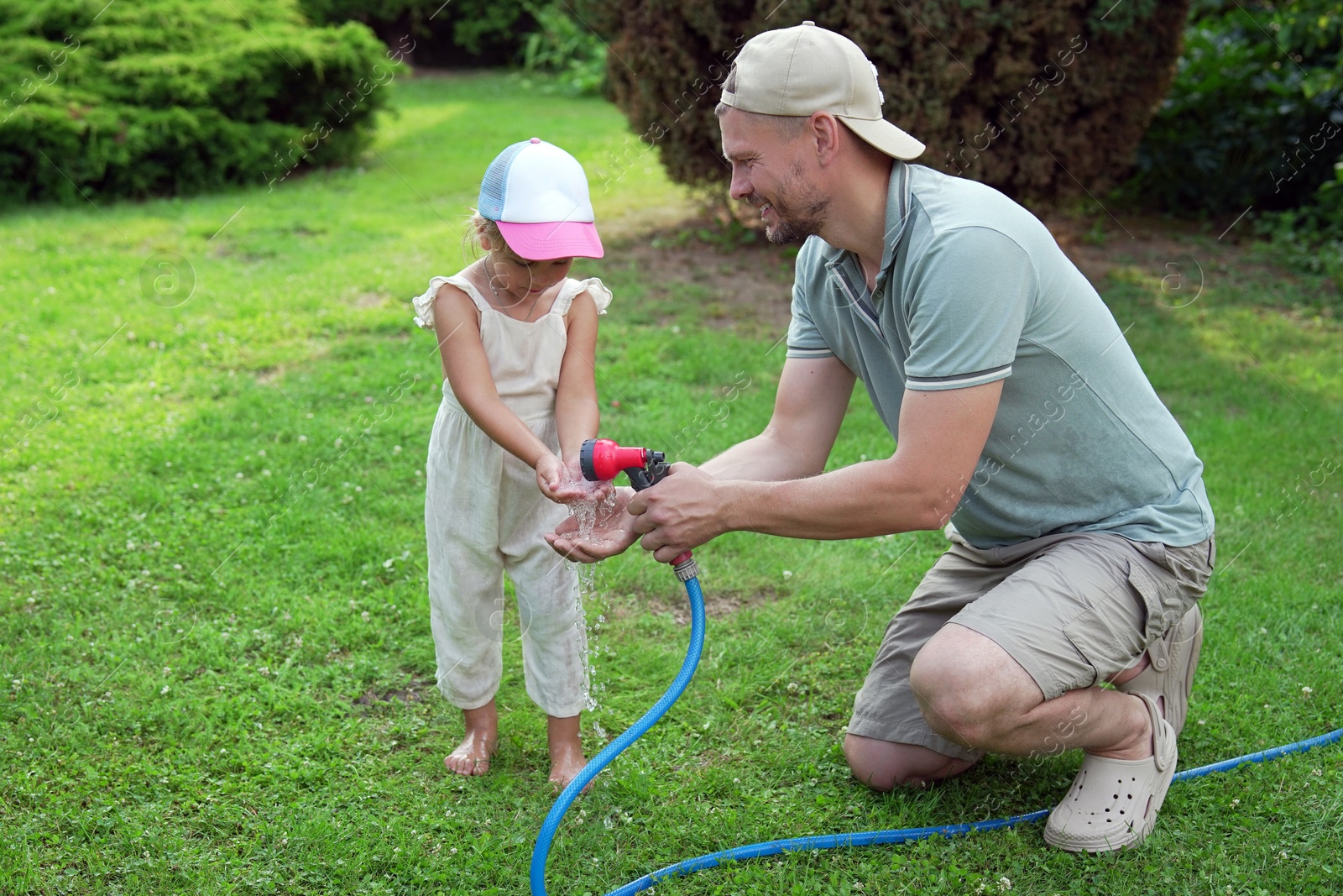 Photo of Father holding hose while his daughter drinking water in backyard