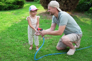 Father holding hose while his daughter drinking water in backyard