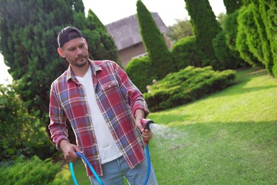 Man watering lawn with hose in backyard, space for text