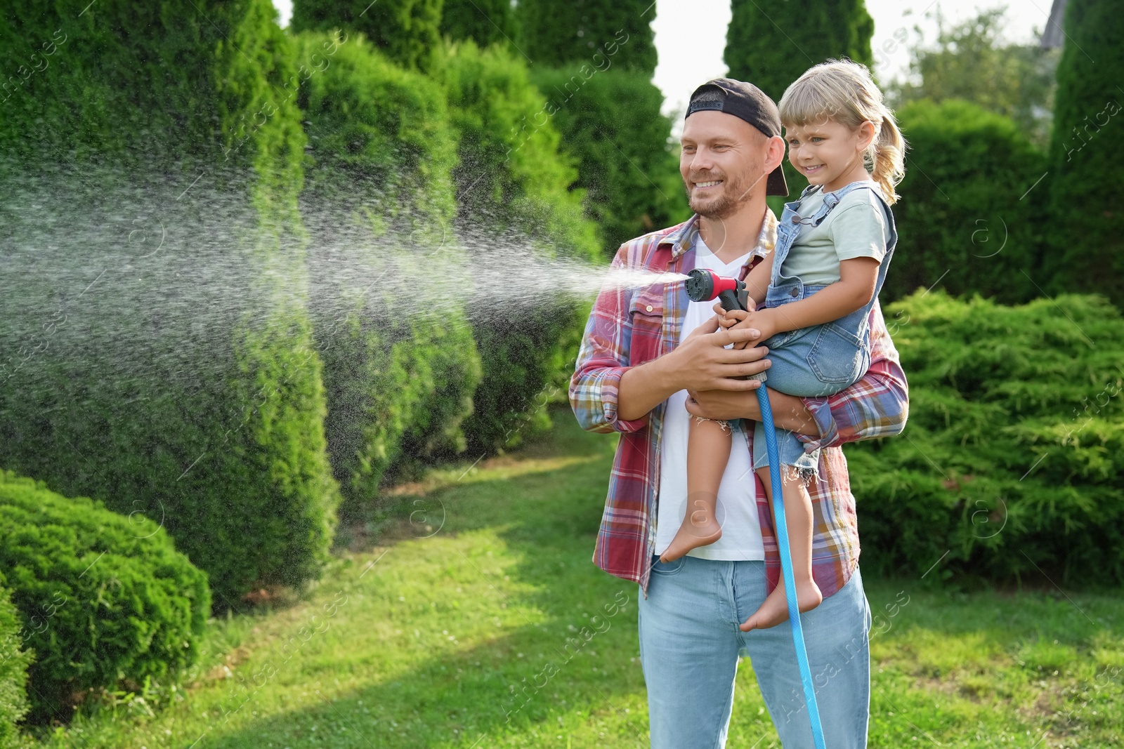 Photo of Father and his daughter watering lawn with hose in backyard