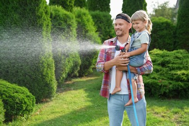 Father and his daughter watering lawn with hose in backyard