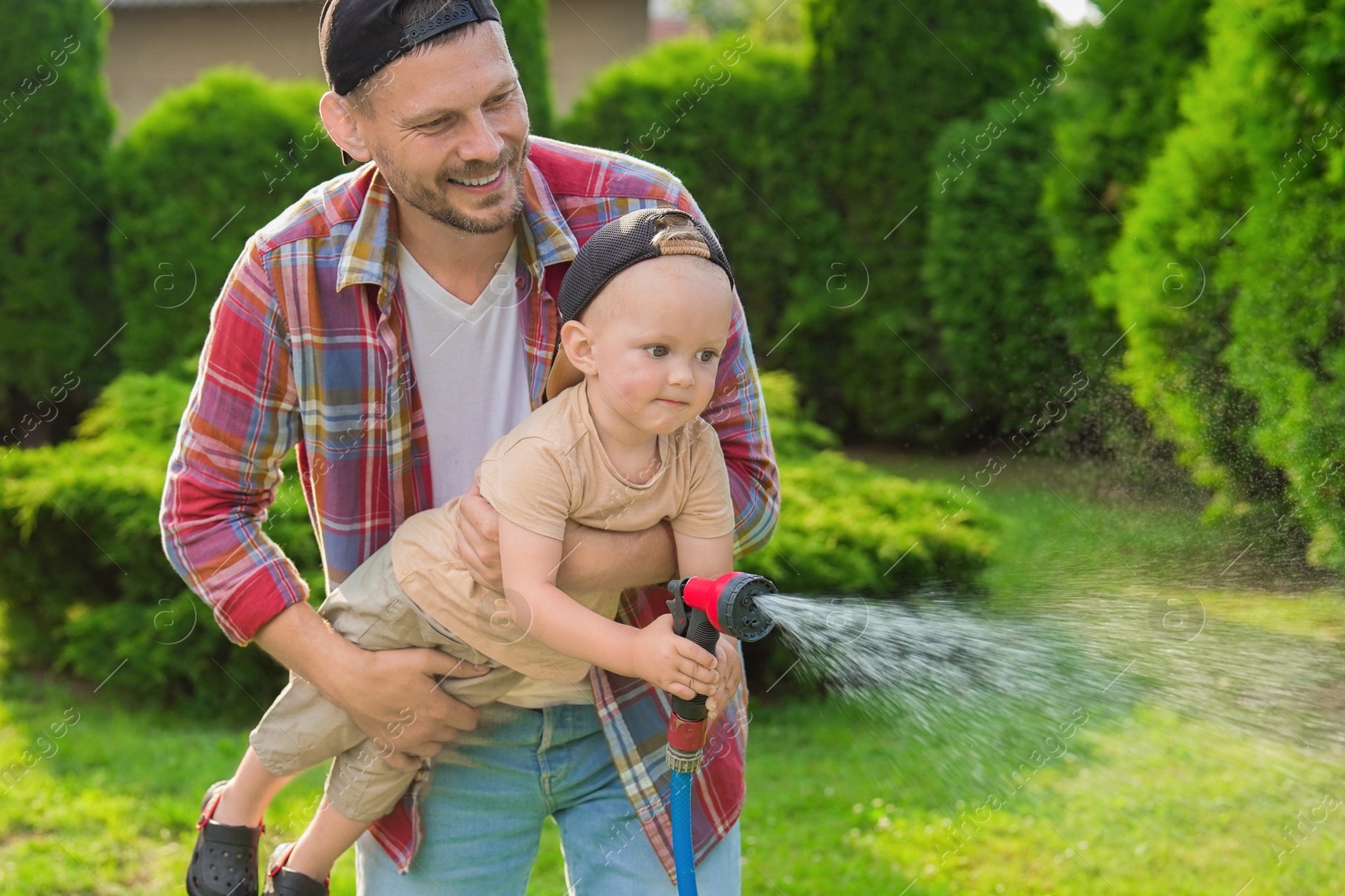 Photo of Father and his son watering lawn with hose in backyard