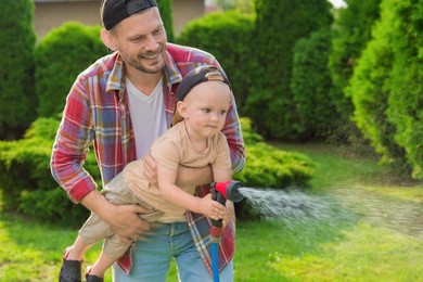 Photo of Father and his son watering lawn with hose in backyard