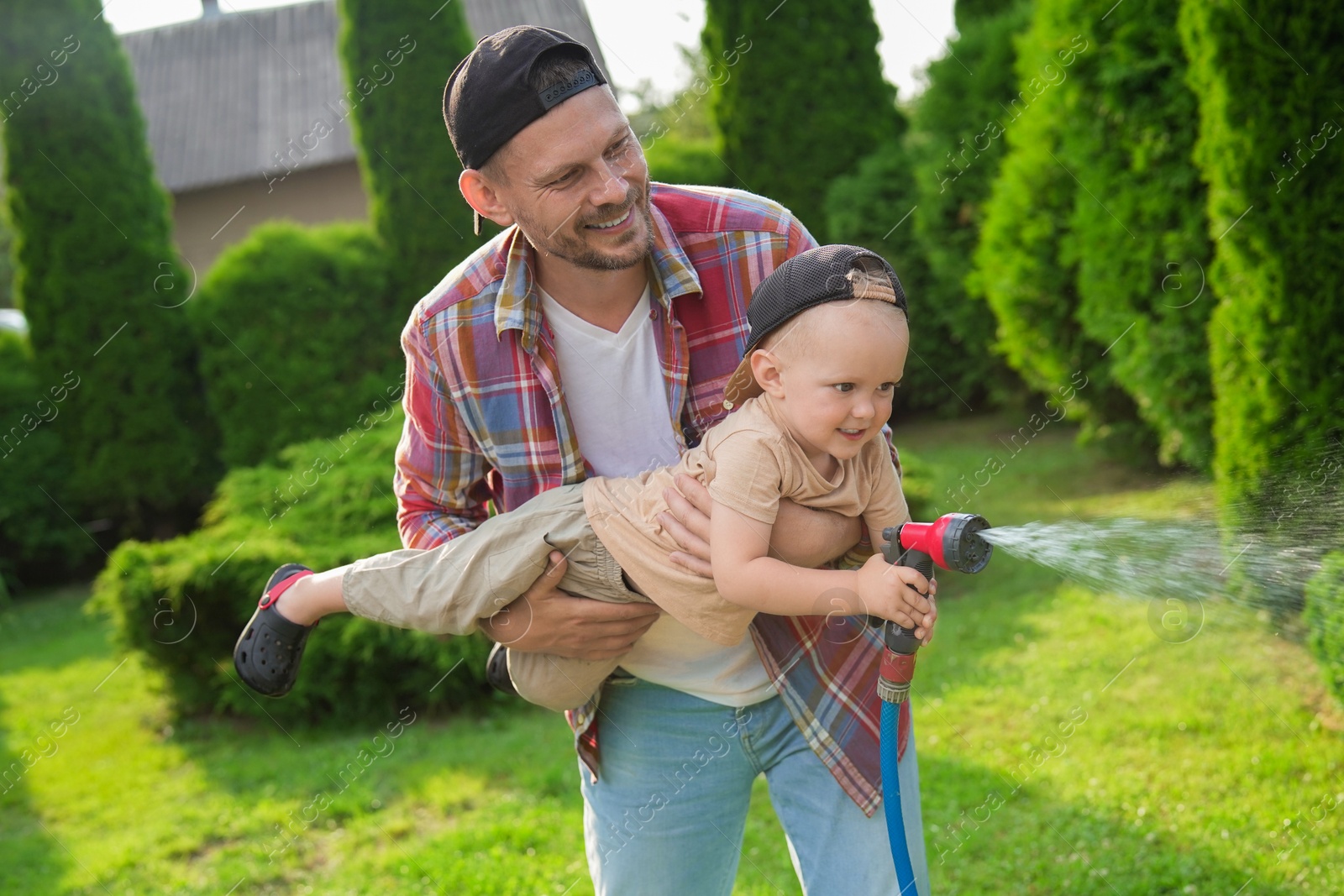 Photo of Father and his son watering lawn with hose in backyard