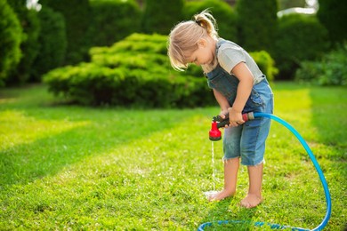 Little girl watering green grass on lawn in backyard, space for text