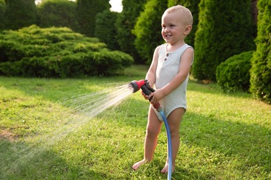 Photo of Little boy watering green grass on lawn in backyard