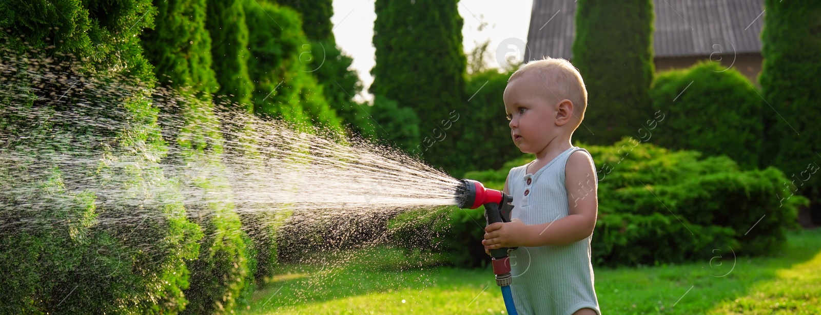 Photo of Little boy watering lawn with hose in backyard