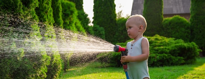 Little boy watering lawn with hose in backyard