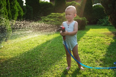 Photo of Little boy watering lawn with hose in backyard