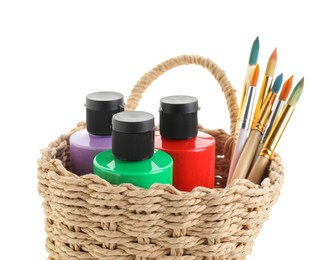 Photo of Acrylic paints of different colors and brushes in wicker basket isolated on white