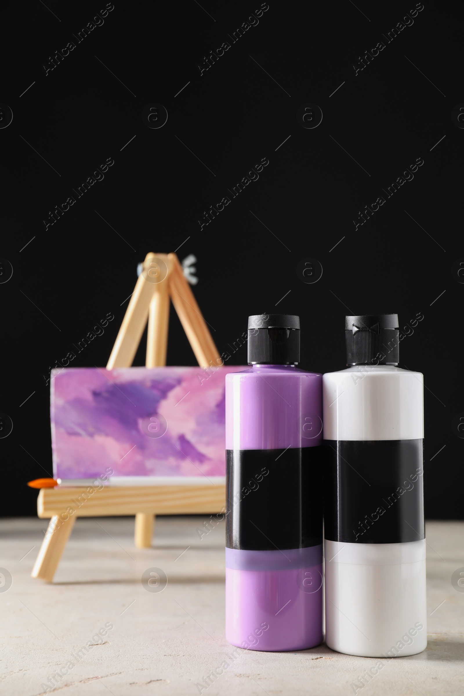 Photo of Acrylic paints of different colors in bottles, brush and small easel with abstract picture on light table