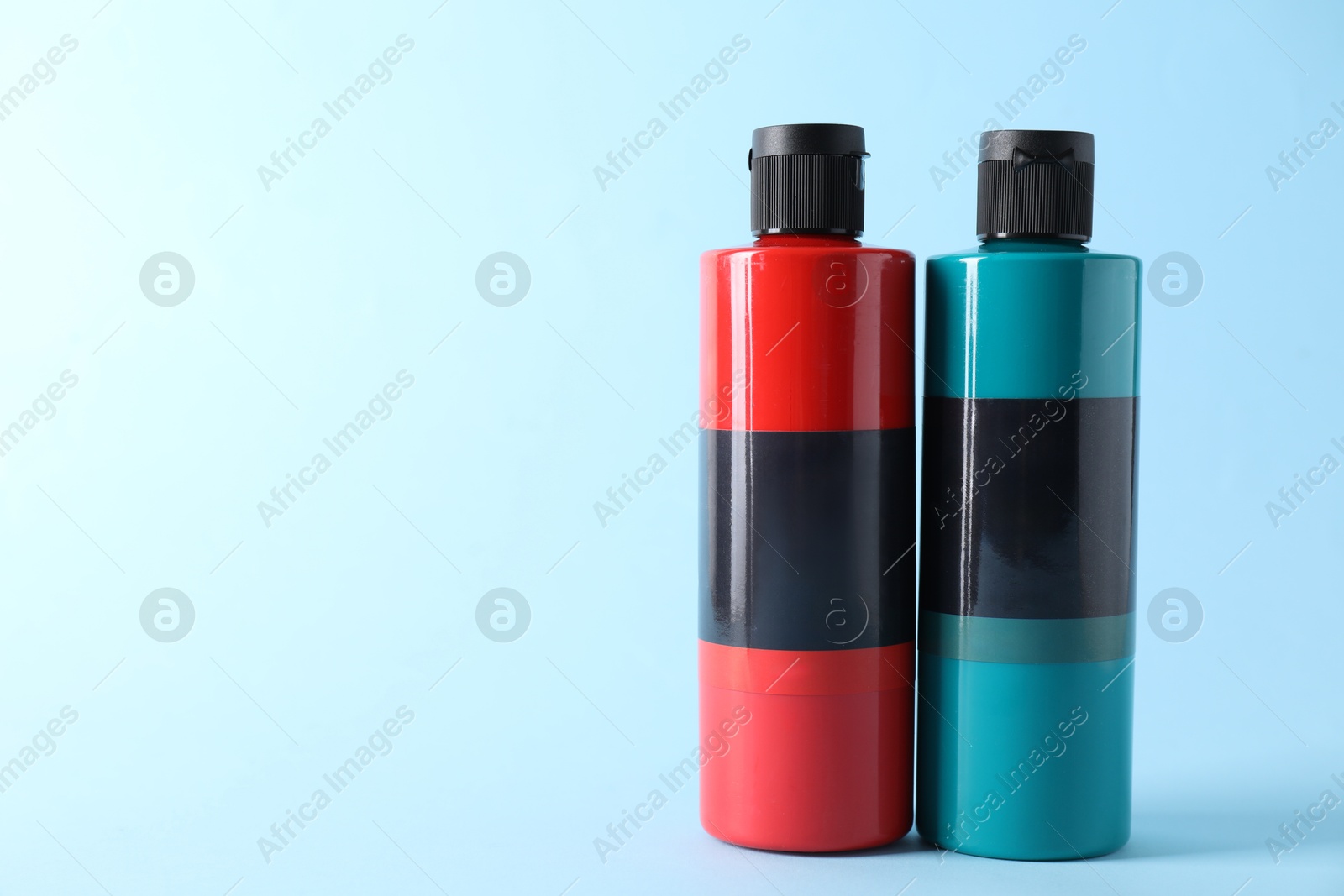 Photo of Acrylic paints of different colors on light blue background, space for text