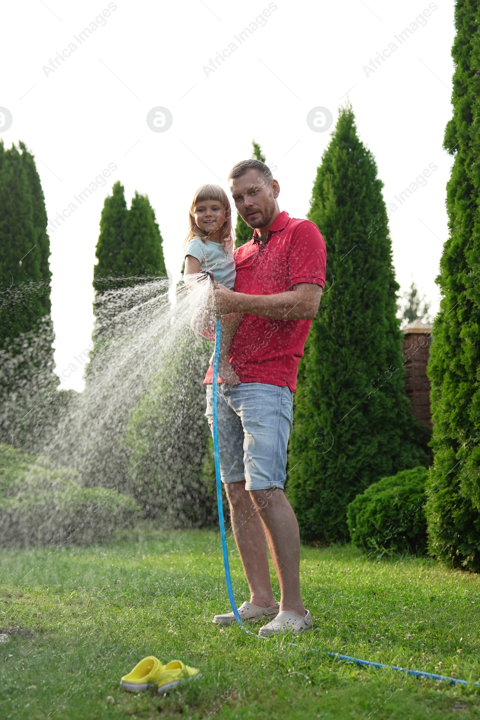 Photo of Father and his daughter watering lawn with hose in backyard