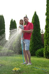 Father and his daughter watering lawn with hose in backyard