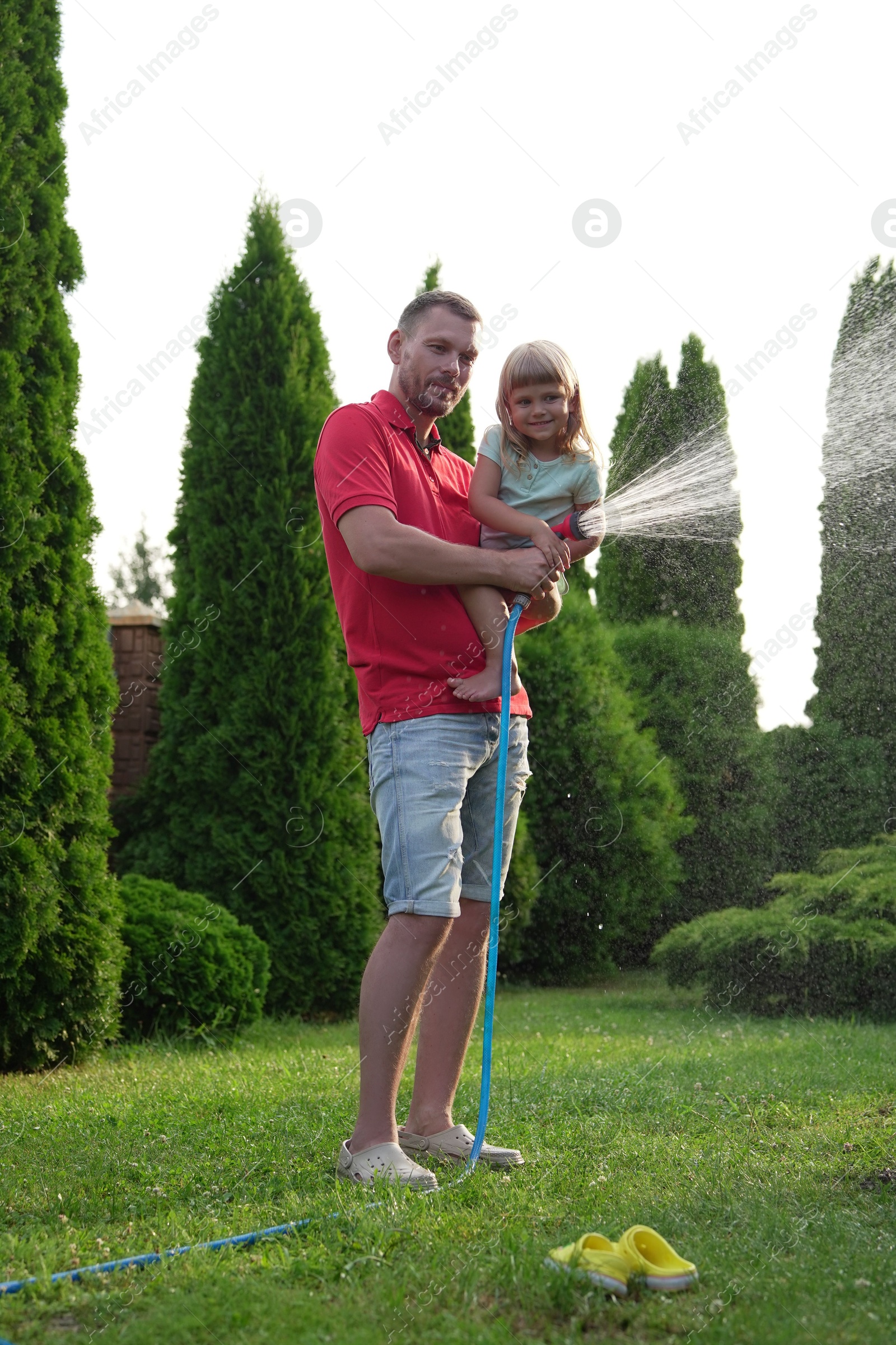 Photo of Father and his daughter watering lawn with hose in backyard