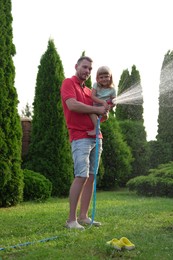 Father and his daughter watering lawn with hose in backyard