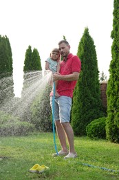 Father and his daughter watering lawn with hose in backyard