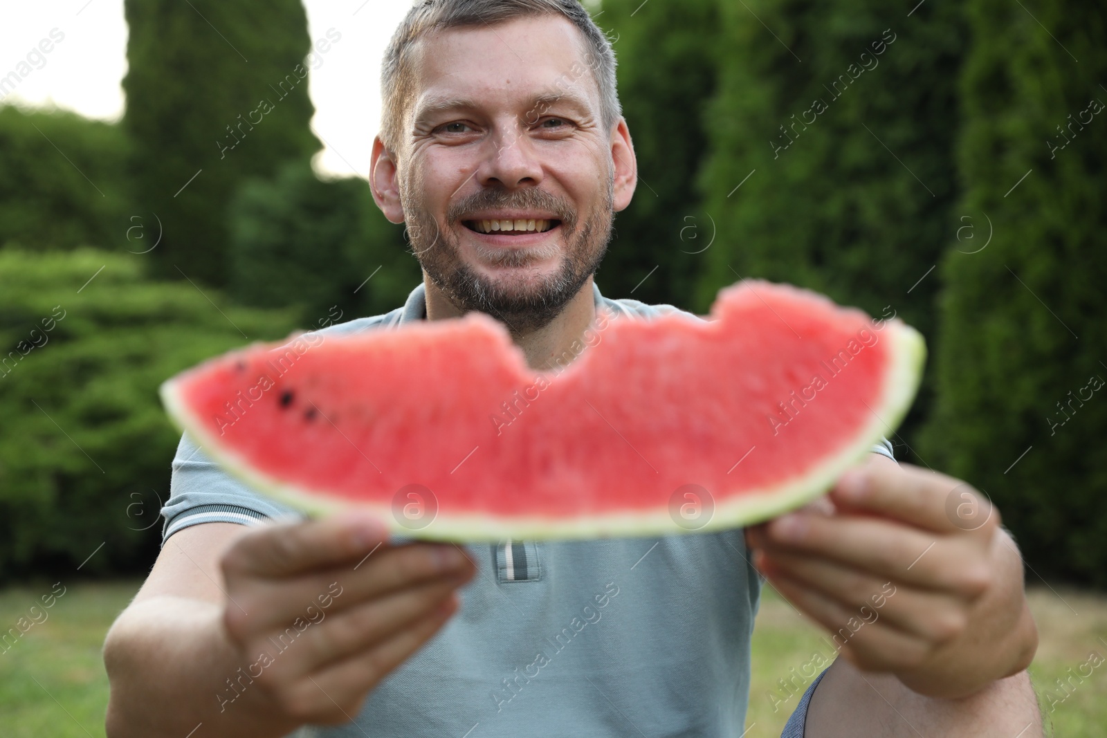 Photo of Happy man with slice of juicy watermelon outdoors