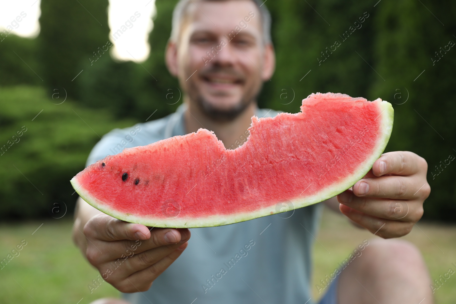 Photo of Happy man with slice of juicy watermelon outdoors, selective focus