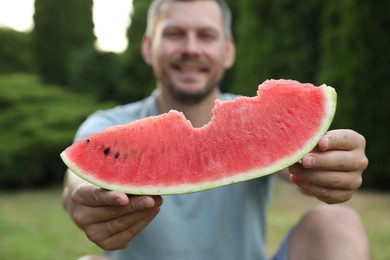 Happy man with slice of juicy watermelon outdoors, selective focus