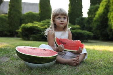 Photo of Cute little girl eating juicy watermelon on green grass outdoors