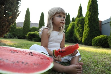 Photo of Cute little girl eating juicy watermelon on green grass outdoors