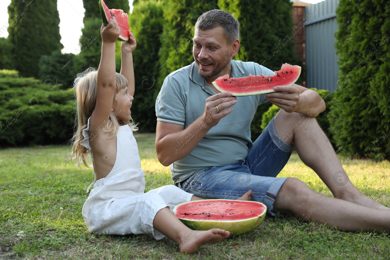 Photo of Man and his cute daughter eating juicy watermelon outdoors together