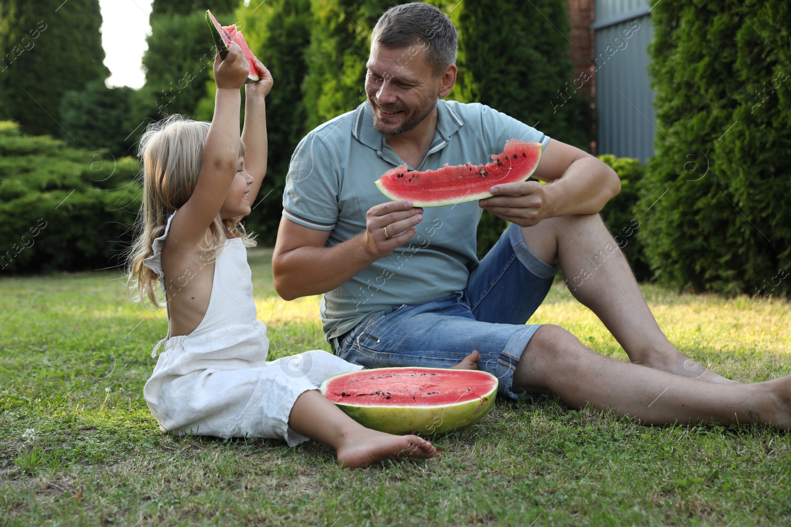 Photo of Man and his cute daughter eating juicy watermelon outdoors together