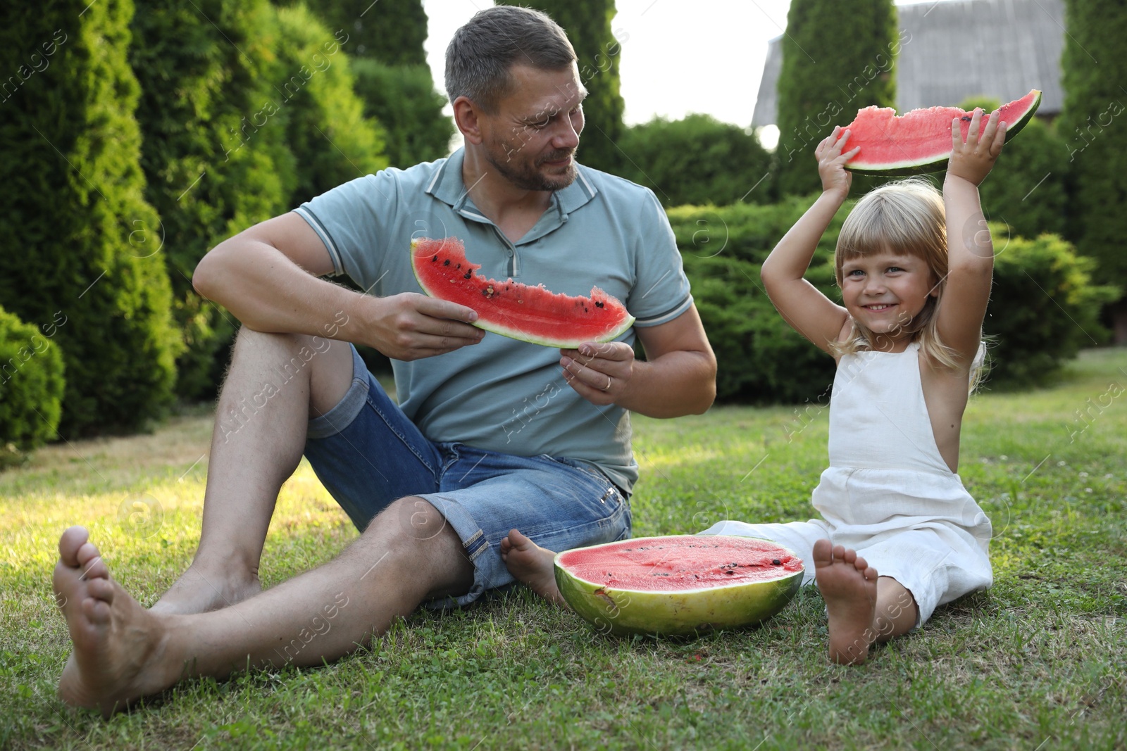 Photo of Man and his cute daughter eating juicy watermelon outdoors together