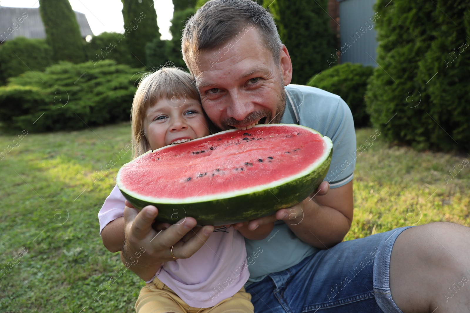 Photo of Man and his cute daughter eating juicy watermelon outdoors together